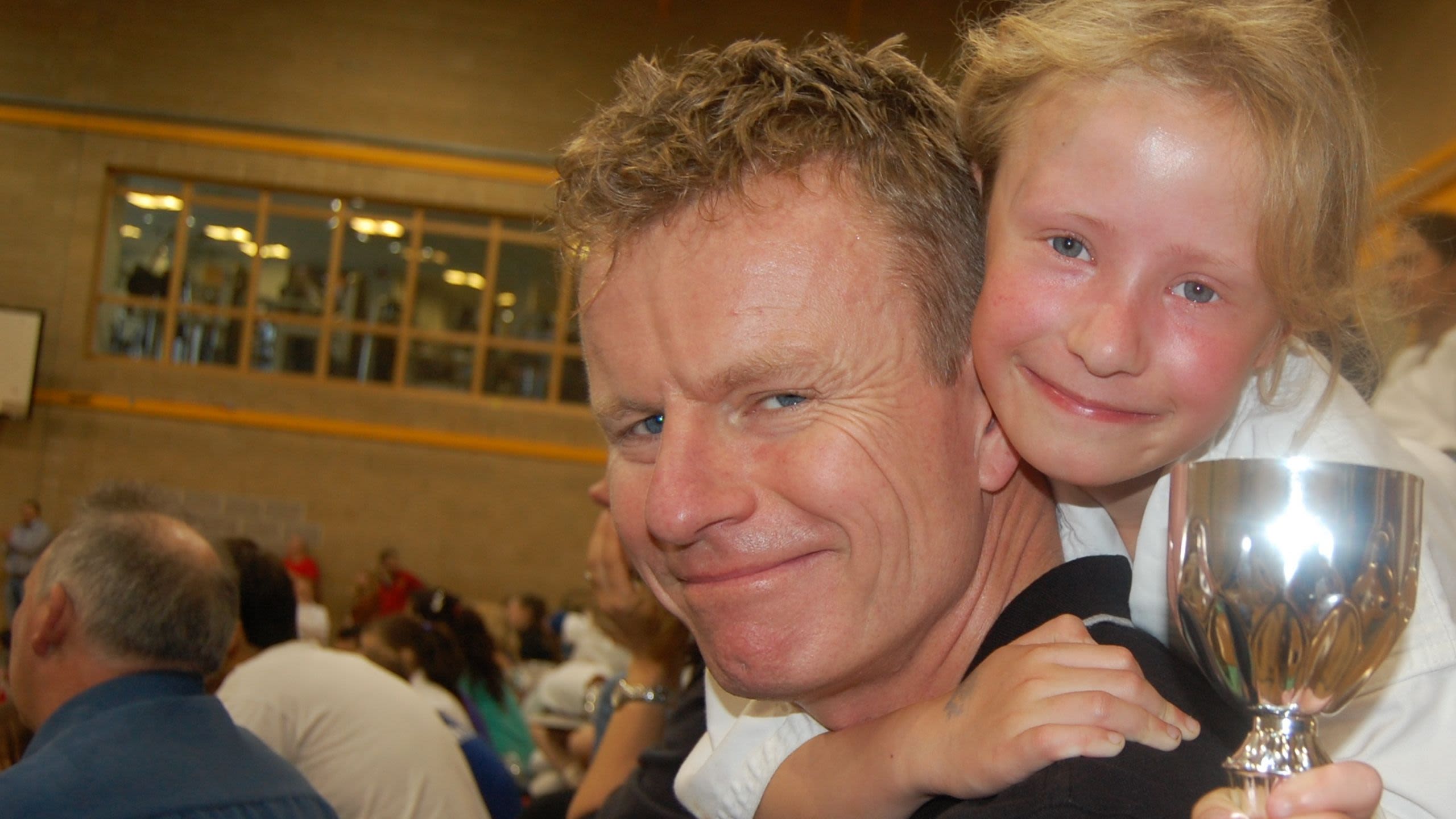 A young Jess hugging her dad and holding a trophy she won at karate