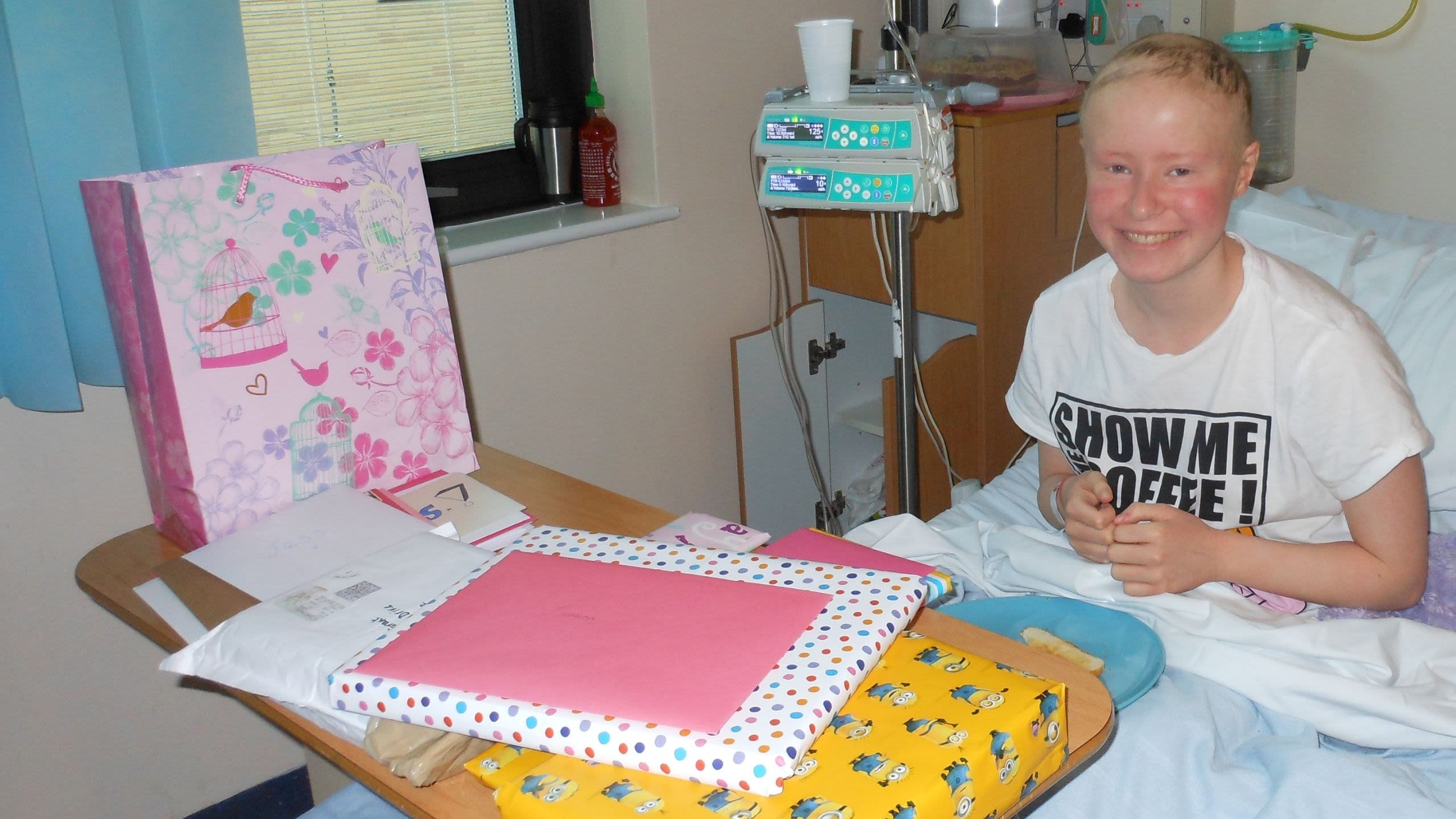 Jess in her hospital bed, smiling and surrounded by birthday presents