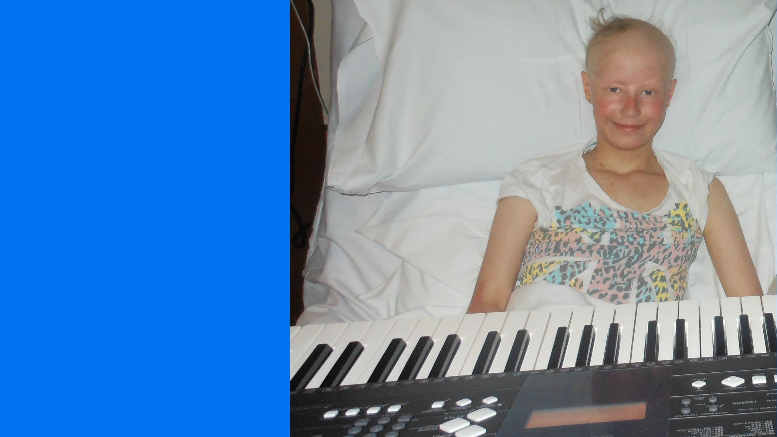 Jess in her hospital bed, smiling, with a keyboard on her lap during a music therapy session